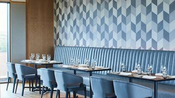 Restaurante moderno com um balcão comprido, cabines estofadas em azul e parede com padrão geométrico.
