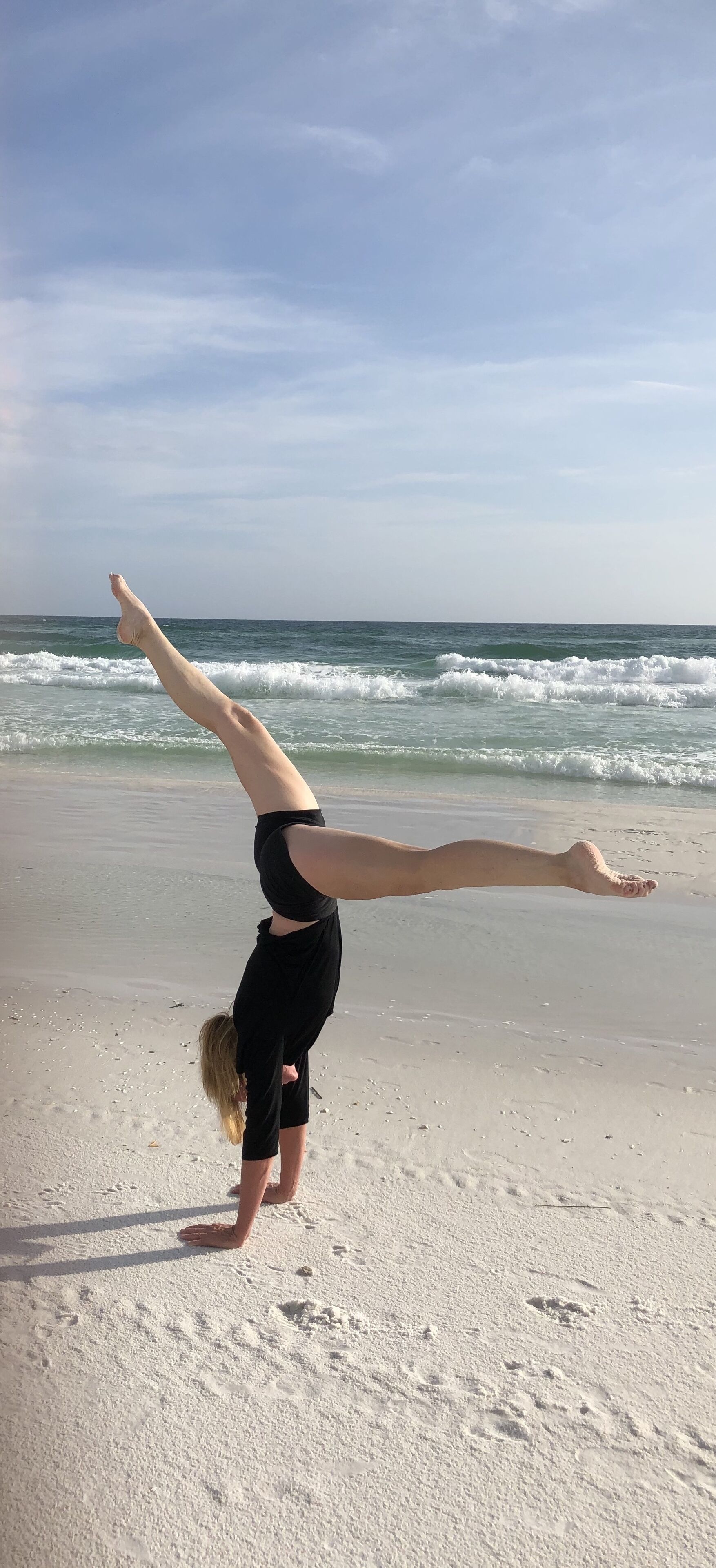 A person performing a handstand on a sandy beach with ocean waves in the background.