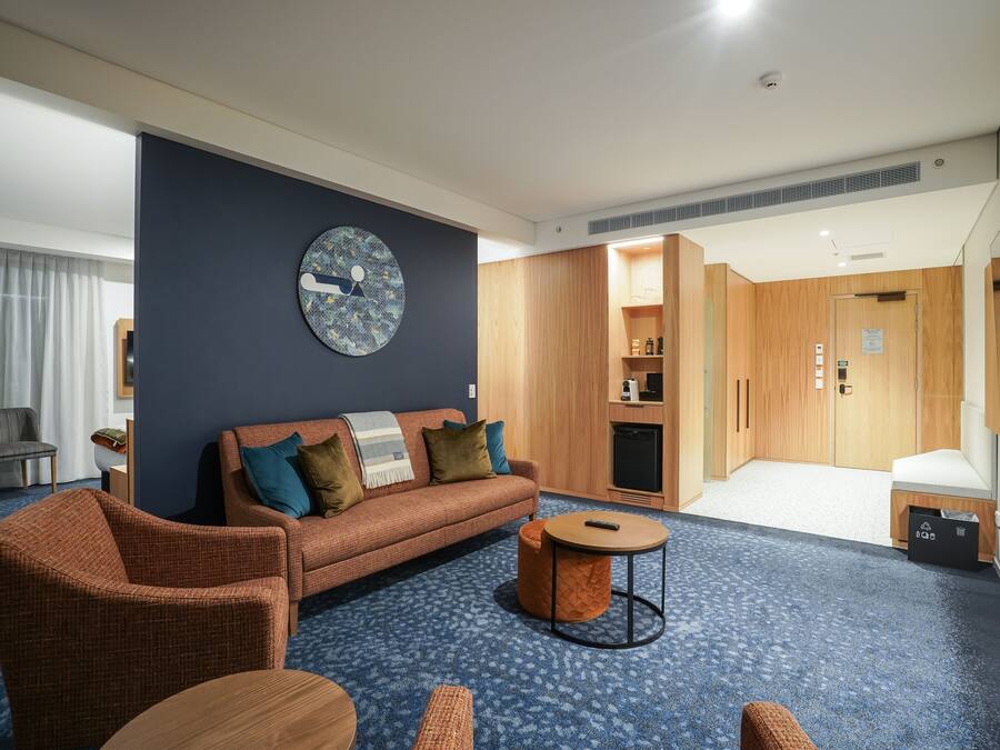 A modern hotel room with a blue carpet, a sofa, a round coffee table, and a large wall clock.