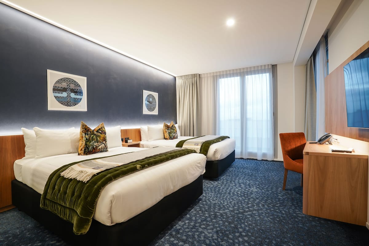 Ein Hotelzimmer mit zwei Betten, einem Schreibtisch und einem großen Fenster mit Vorhängen.