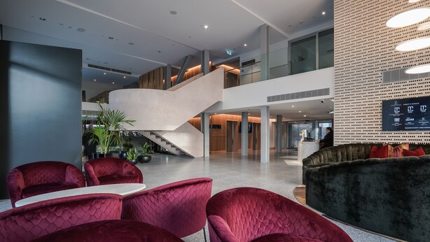 A spacious lobby with a modern staircase, red upholstered seating, and a digital display on the wall. - The Langlands Hotel (Invercargill)