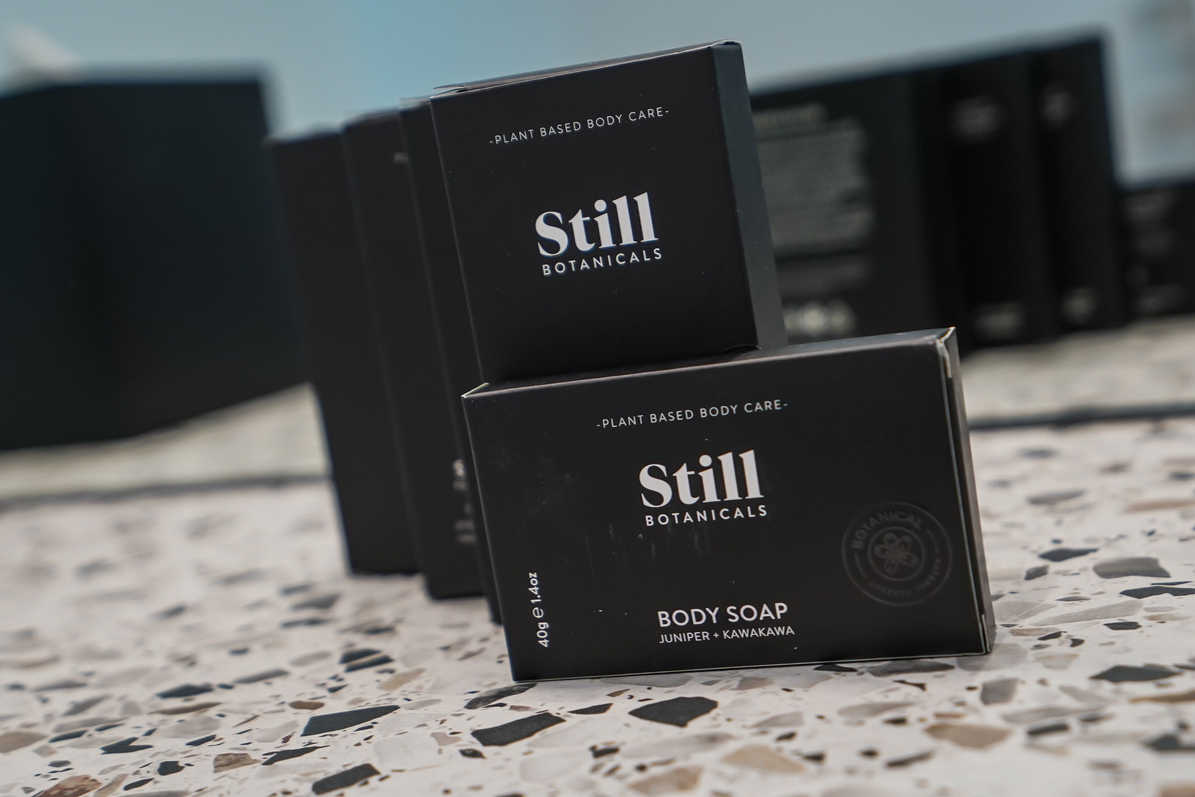 A series of black boxes labeled "Still Botanicals" on a terrazzo floor.
