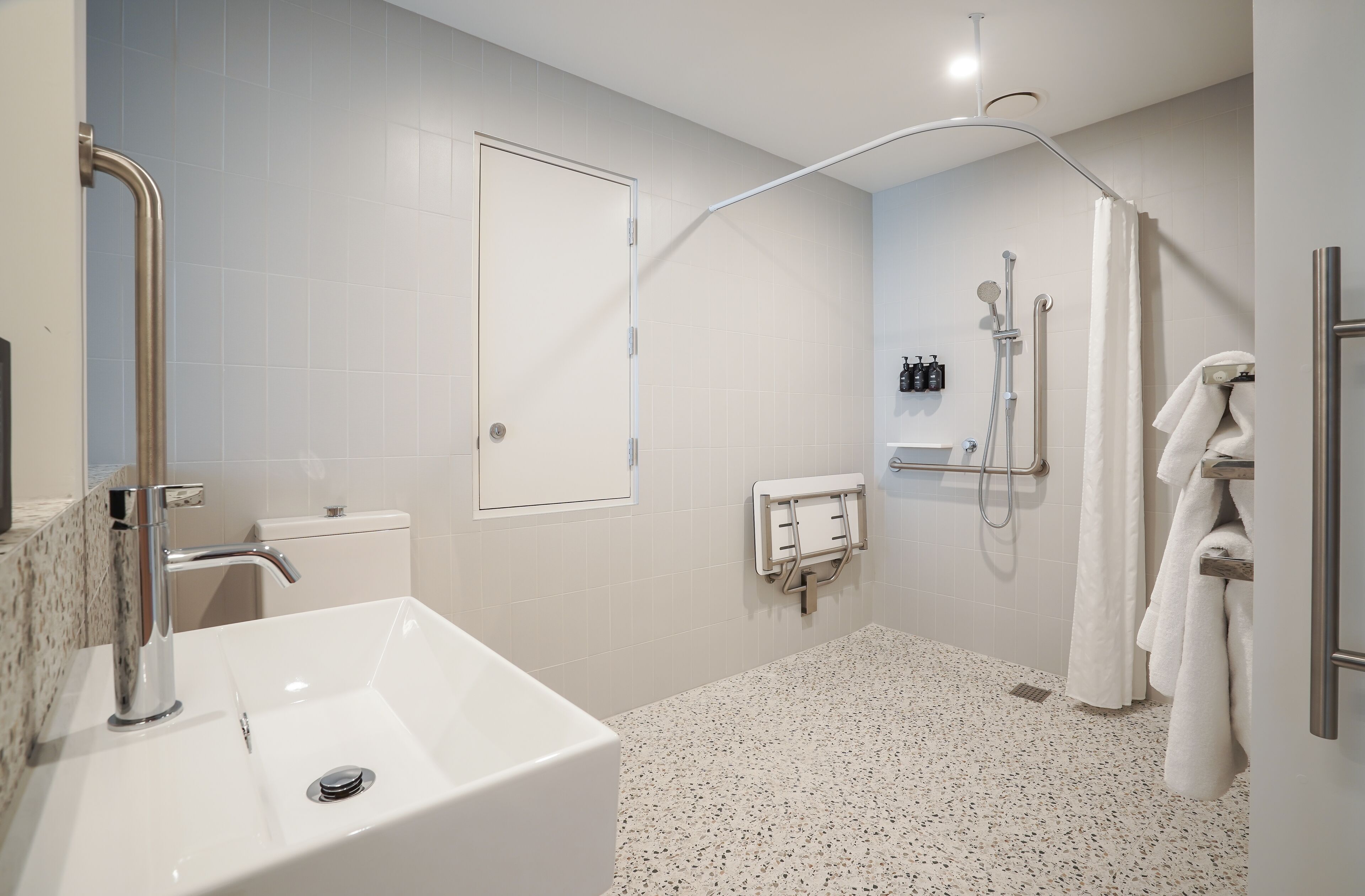 A modern bathroom with a white sink, a shower with a handheld showerhead, and a towel rack.