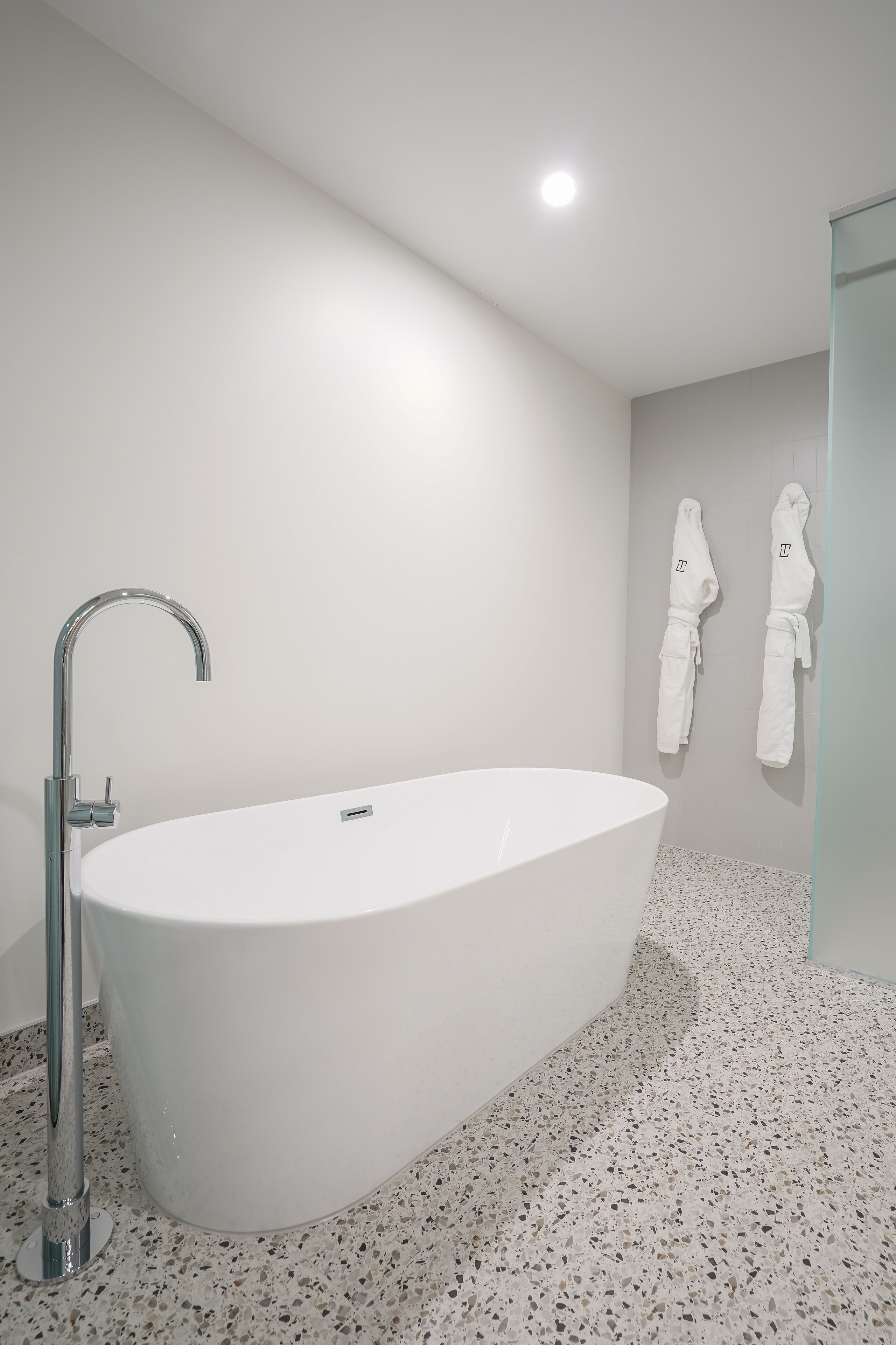 A modern bathroom with a freestanding bathtub, a chrome faucet, and two white towels hanging on the wall.