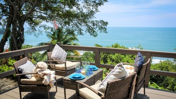 Eine Terrasse mit Korbmöbeln, einem Tisch gedeckt mit blauen Tellern und Gläsern, und Blick auf das Meer.
