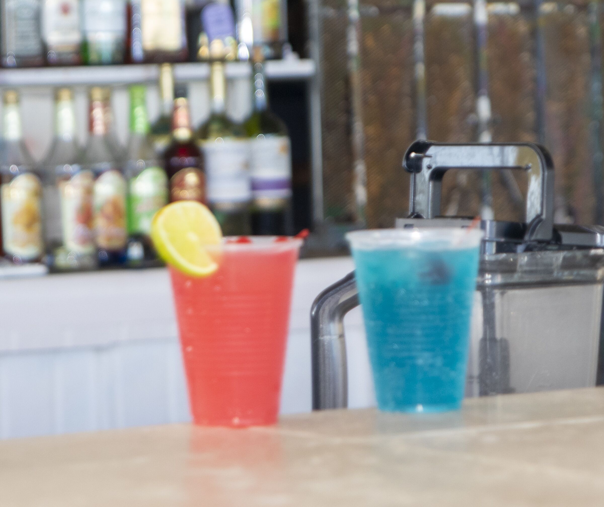 Two drinks on a bar counter with a blurred background of bottles.