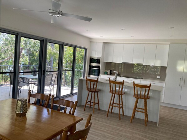 A modern kitchen with white cabinets, a dining area with wooden chairs, and a large sliding glass door leading to an outdoor patio.