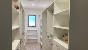 Un petit dressing étroit, doté de nombreuses étagères et de tiroirs, avec une fenêtre au fond et un plancher en bois de couleur claire.
