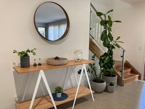 A modern interior with a wooden console table, a round mirror, and potted plants.
