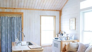 Interior de una cabaña de madera con cocina, comedor y un amplio ventanal.
