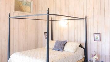 Una cama con dosel, un pequeño mesita de noche con mantel estampado y un tapiz decorativo.