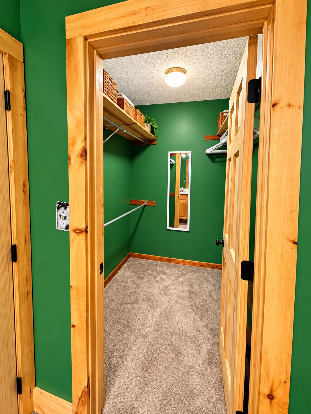 Habitació amb parets verdes, una porta de fusta, un mirall i una prestatgeria amb cistells.