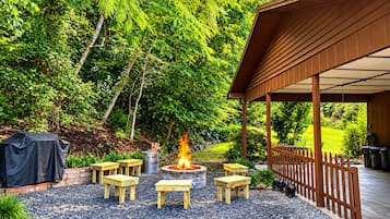 An outdoor patio with a fire pit, wooden tables, and a covered seating area.