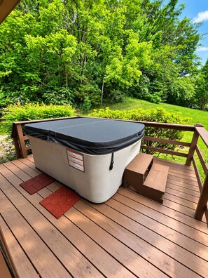 A hot tub on a wooden deck with a railing, surrounded by lush greenery. - Cozy Cabin Retreat Sleeps 12 w/ HotTub, Wi-Fi, FirePit minutes from Dollywood!! (Sevierville)