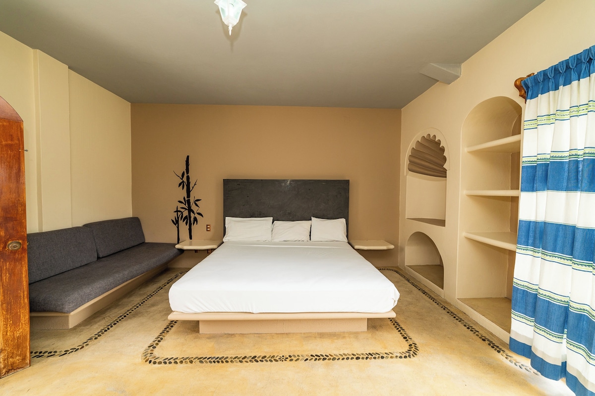 Une chambre à coucher comprenant un lit, un canapé, une plante décorative et une bibliothèque.