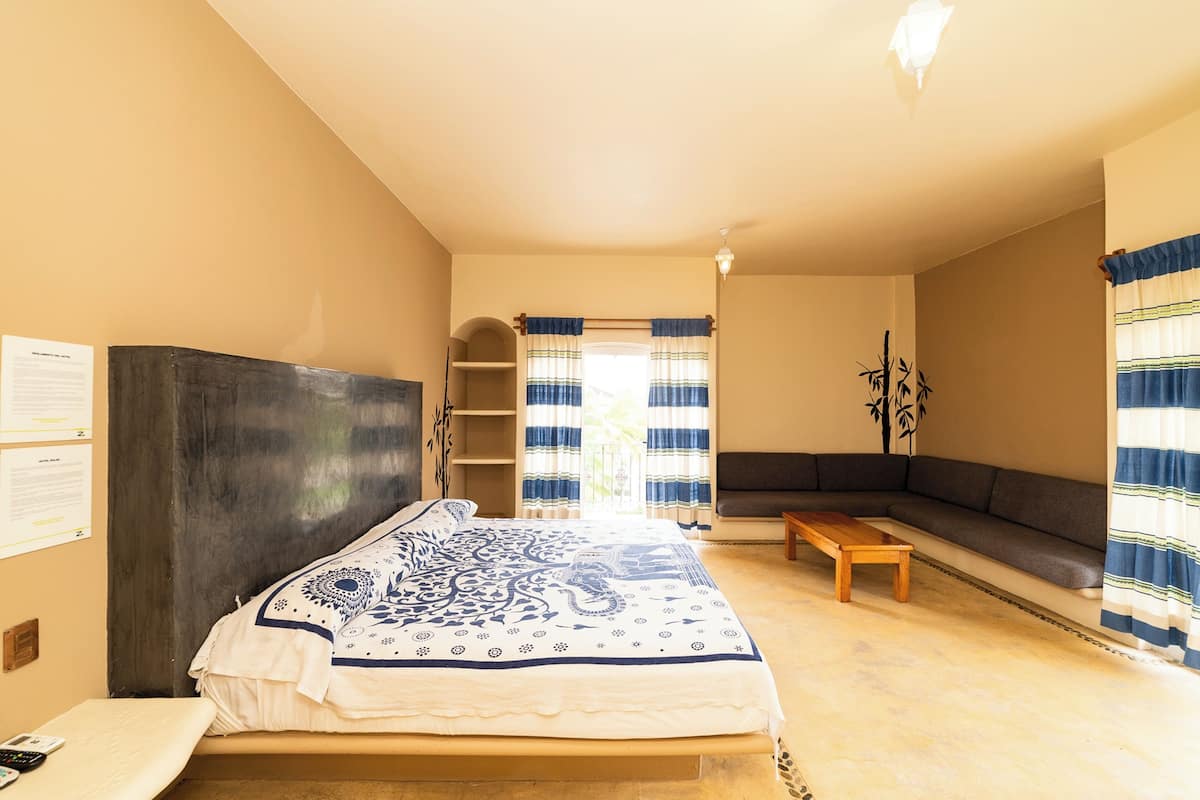 Une chambre à coucher avec un lit, un banc, un canapé et une fenêtre avec des rideaux.