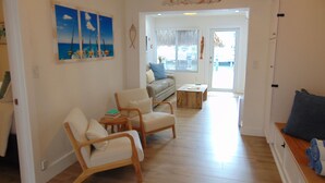 A spacious living room with a wooden floor, a sofa, two armchairs, and a coffee table. There are paintings on the wall and a door leading to another room. - Little Island Pearl (Key Colony Beach)