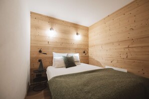 A bedroom with a wooden wall, a bed with pillows, a bedside table, and a lamp.