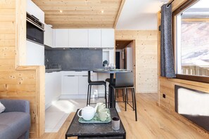 A compact kitchen with white cabinets, a black countertop, and a wooden ceiling. There is a dining area with a table and chairs, and a window with a view of the outdoors.