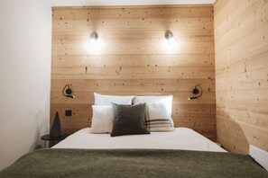 Een slaapkamer met een houten hoofdbord, twee bedlampen, een bed met kussens en een klein nachtkastje met een lamp.