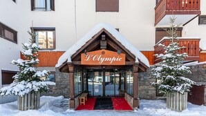 A hotel entrance with a sign reading "L'Olympic," wooden balconies, and snow-covered trees.