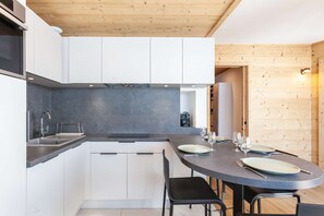 A modern kitchen with white cabinets, a dark countertop, and a wooden ceiling.