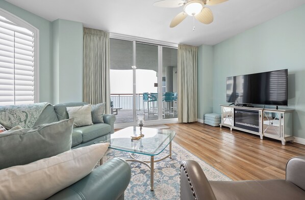 A living room with a sofa, a glass coffee table, a television on a cabinet, and a balcony with sliding doors.