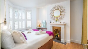 A bedroom with a large bed, a fireplace, and a window with shutters. - Stylish flat with private yard in Shepherd’s Bush (London)