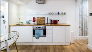 A modern kitchen with white cabinetry, a wooden countertop, and a built-in oven. - Stylish flat with private yard in Shepherd’s Bush (London)