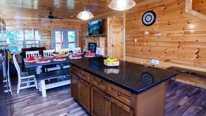 A wooden interior with a kitchen area featuring a dining table, chairs, and a central island with a fruit bowl. - ☆Fun Cabin!☆Private Indoor Pool☆Hot Tub☆Game Room☆Zipline☆Fast WiFi☆Near PF (Sevierville)