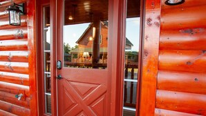 Una cabaña roja de madera con una puerta doble, un felpudo y dos faroles en el porche.