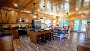 Una cocina amplia con armarios de madera, una isla central con taburetes, electrodomésticos de acero inoxidable y un comedor con vistas al exterior.