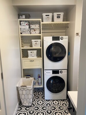 A laundry room with two stacked washing machines, a drying rack, and storage baskets on shelves. - Bozeman Beehive (Bozeman)