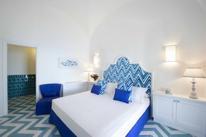 A hotel room with a large bed, a blue chair, a wall-mounted lamp, and a decorative wall piece. - MyExclusiveItaly - Exclusive Villa in Praiano with Pool & View (Praiano)