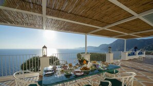 An outdoor dining area with a table set for a meal, overlooking a scenic view of the sea and mountains. - MyExclusiveItaly - Exclusive Villa in Praiano with Pool & View (Praiano)