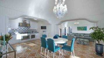 A spacious living area with a round dining table, teal chairs, and a chandelier.
