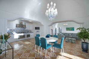 Amplia sala de estar con una mesa redonda de comedor, sillas color turquesa y una lámpara de araña.