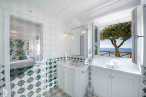 A bathroom with a large window, a sink, a mirror, and a view of the sea.