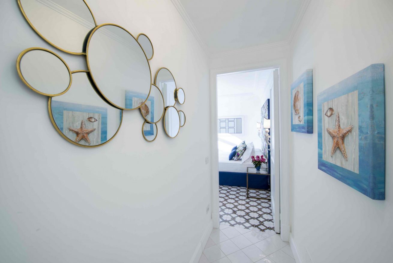 A hallway with a white tiled floor, a door leading to a bedroom, and wall-mounted starfish paintings.