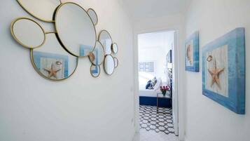 A hallway with a white tiled floor, a door leading to a bedroom, and wall-mounted starfish paintings.