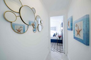 A hallway with a white tiled floor, a door leading to a bedroom, and wall-mounted starfish paintings. - MyExclusiveItaly - Exclusive Villa in Praiano with Pool & View (Praiano)