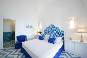 A hotel room with a large bed, a blue chair, a wall-mounted lamp, and a decorative wall piece.