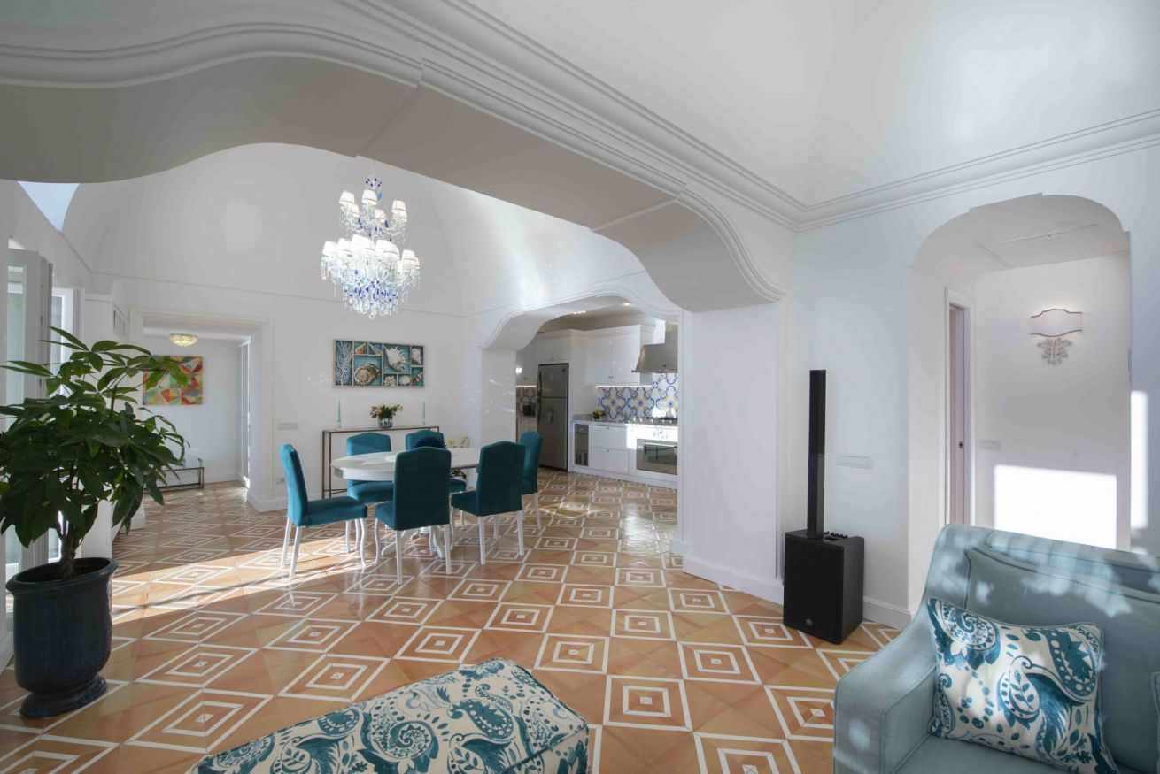 A spacious living area with a dining set, a large potted plant, and a patterned floor.