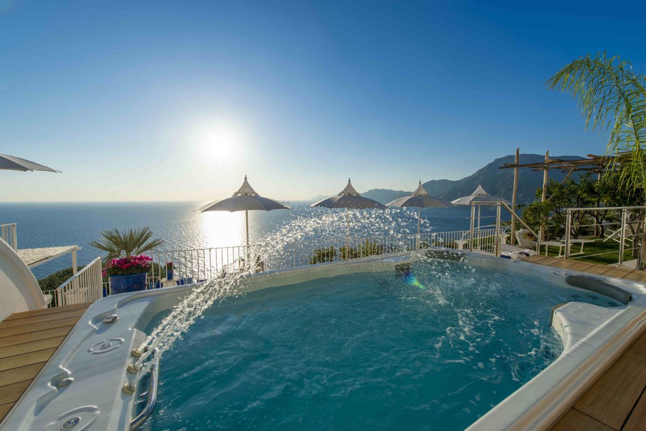 A hot tub with a view of the sea, surrounded by umbrellas and a deck.