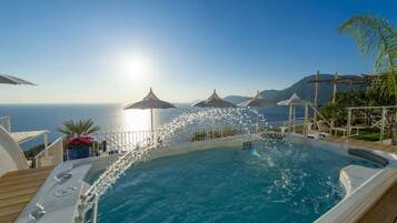 A hot tub with a view of the sea, surrounded by umbrellas and a deck.