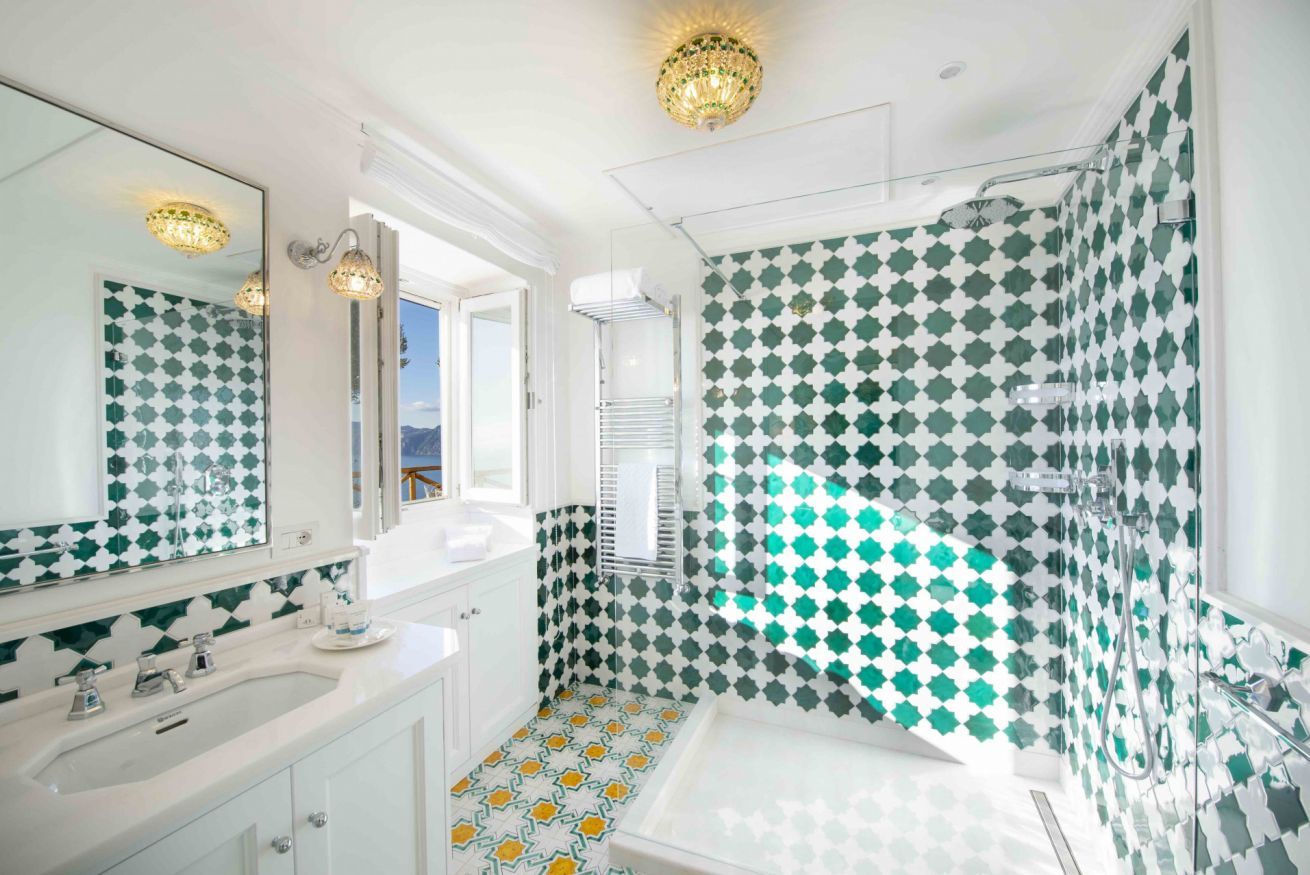 A bathroom with a white sink, a large mirror, and a shower area with green and white patterned tiles.