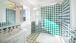 Une salle de bain avec un lavabo blanc, un grand miroir et un espace douche dont les carreaux sont décorés de motifs verts et blancs.