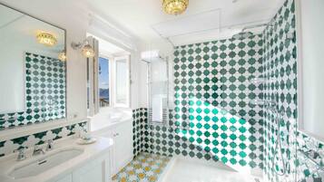 A bathroom with a white sink, a large mirror, and a shower area with green and white patterned tiles.