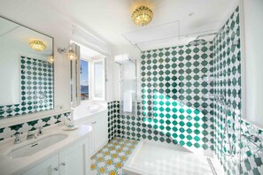A bathroom with a white sink, a large mirror, and a shower area with green and white patterned tiles.