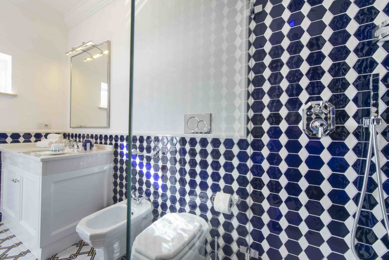 A bathroom with a white vanity, a large mirror, a shower with a glass door, and a blue and white hexagonal tile backsplash.
